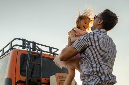 A joyful moment between a father and daughter outdoors with a van in the background.
